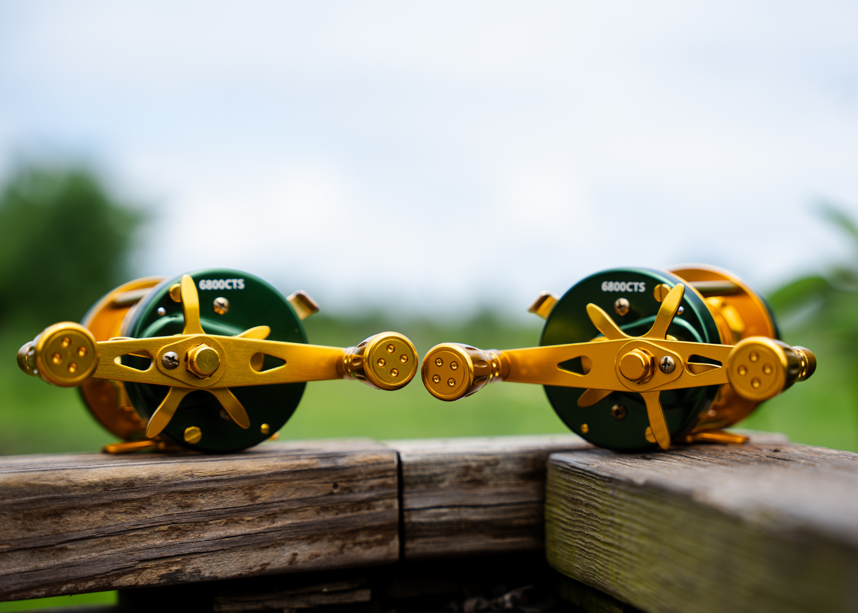Two fishing reels with yellow accents on a wooden surface outdoors.