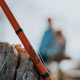 a close shot photo of a Catfish Pro Spinning Rod laying up on a tree with people behind out of focus.