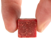 Close-up of a person's fingers holding a single cube of Catfish Pro Beef Blood Square Bait.