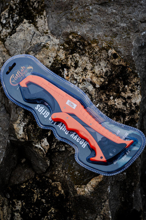 Orange and Black Heavy-Duty Fishing Lip Grippers in package on a rocky surface