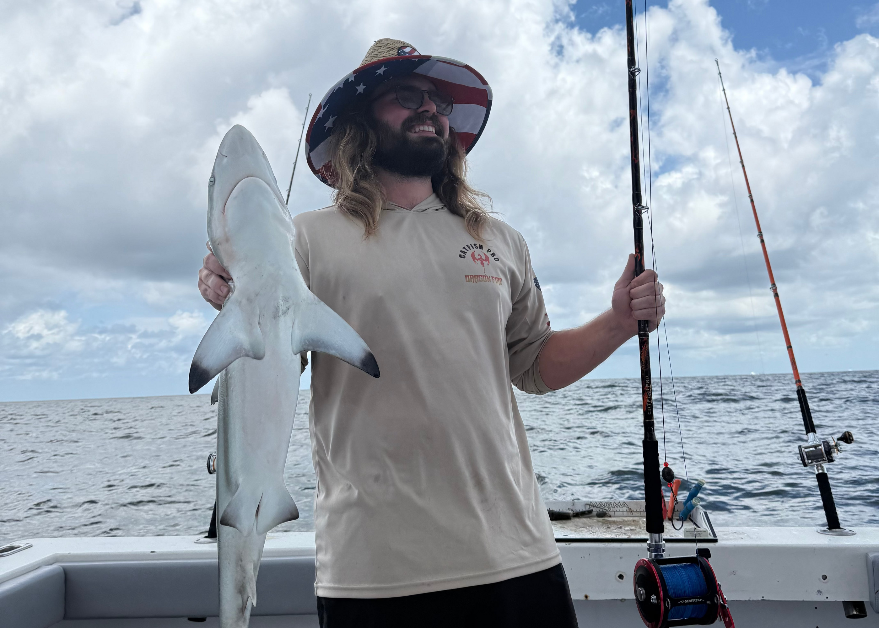 Man holding a shark on a boat with ocean and sky in the background