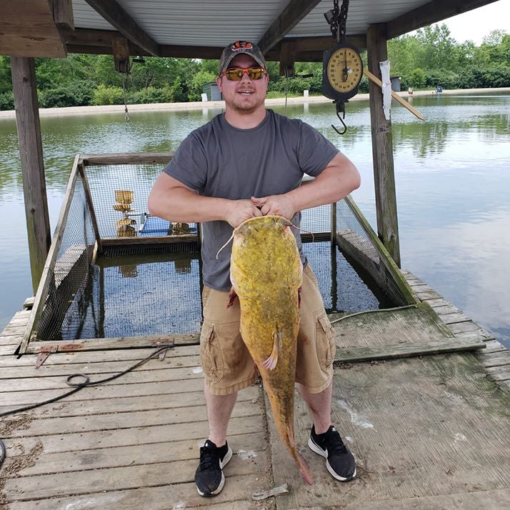 Man holding a large fish on a dock by a lake